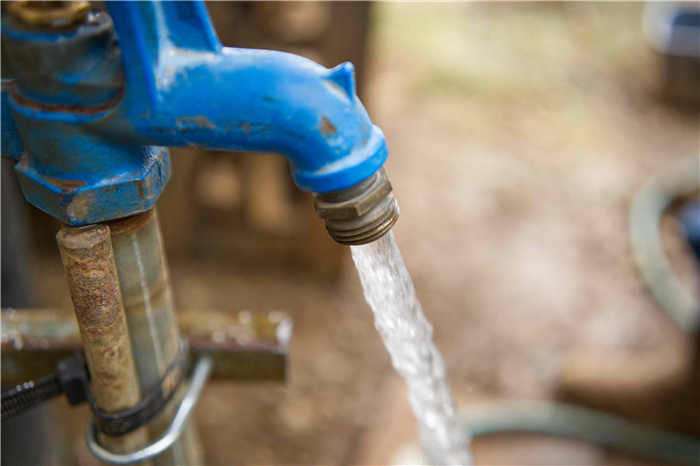 water streams out of blue metal pipe on outdoor farm for goats